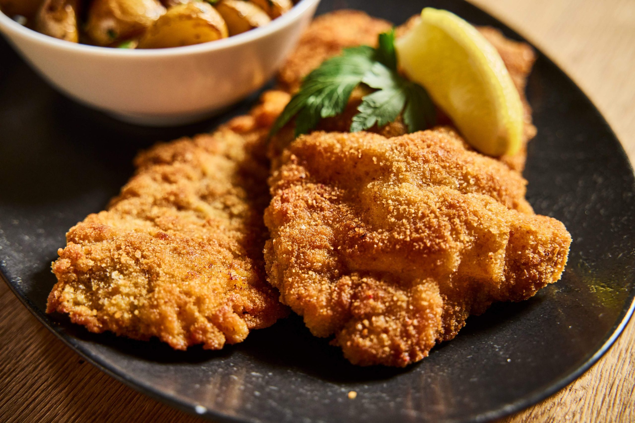 Goldbraunes Schnitzel mit einer Spalte Zitrone, dazu ein Schälchen Ofenkartoffeln