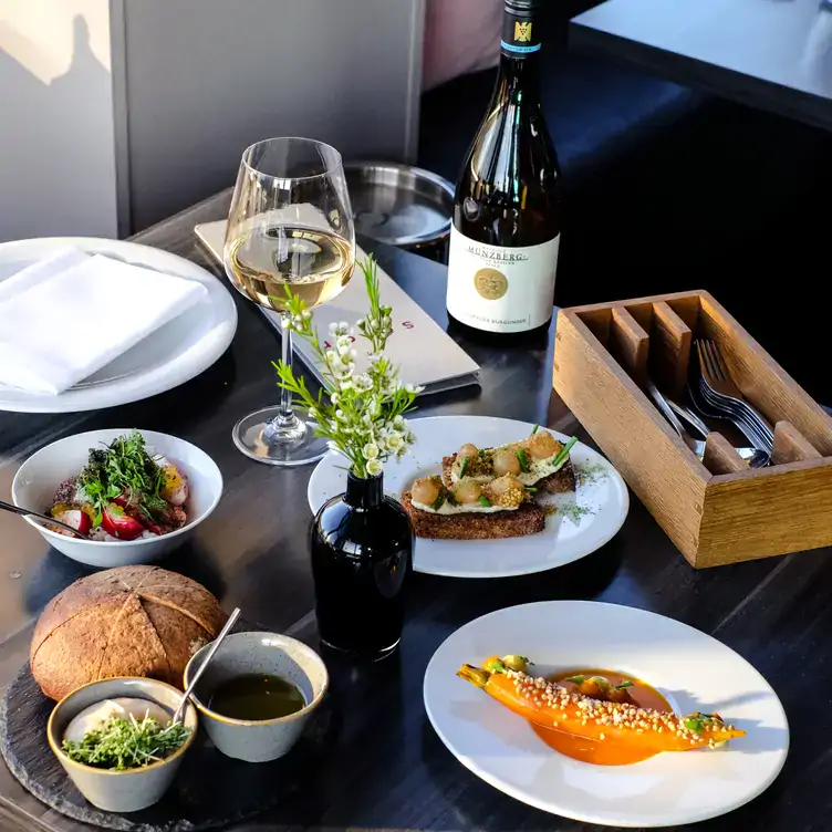 Tisch mit verschiedenen experimentellen Häppchen und einer Flasche Wein im Solar, einer der schönsten Dachterrassen in Berlin.