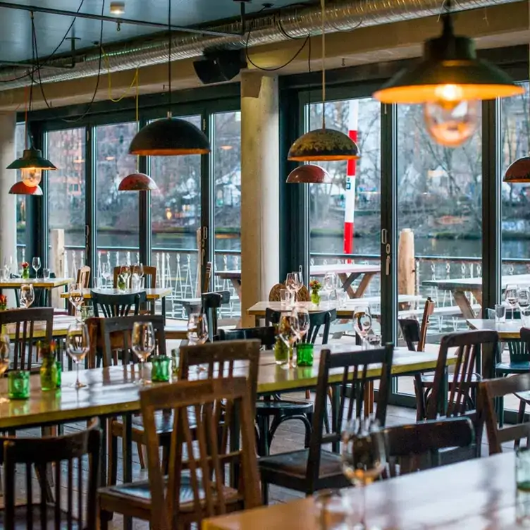 Lichtdurchfluteter Innenbereich mit Tischen und Blick nach draußen im Katerschmaus, einem der besten Restaurants mit Außenplätzen in Berlin.