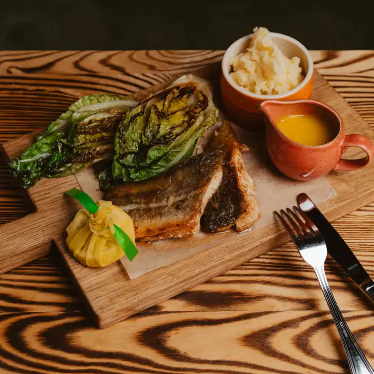 Holzbrett mit paniertem Fischfilet, Kartoffelpüree, Sauce und Kohl im Jäger & Lustig, einem der besten Restaurants mit Außenbereich in Berlin.