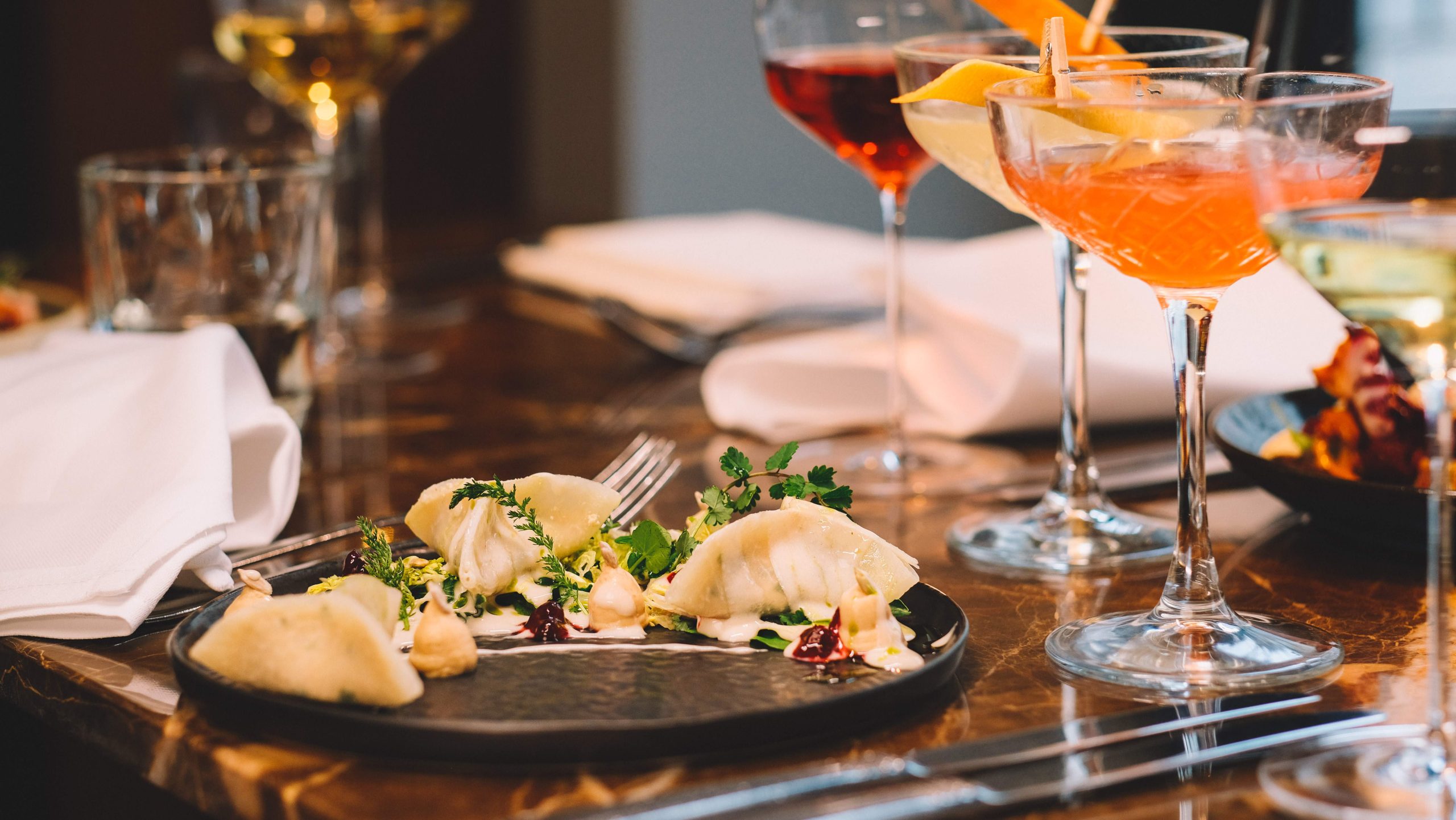 Ein Teller mit Kohlrabi-Ravioli und Cocktailgläser auf einem dunklen Marmortisch