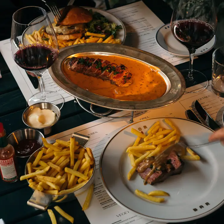 Gedeckter Tisch mit saftigem Burger und Entrecôte, dazu Pommes Frites und ein Glas Rotwein in der TORBAR, einem der besten französischen Restaurants in Berlin