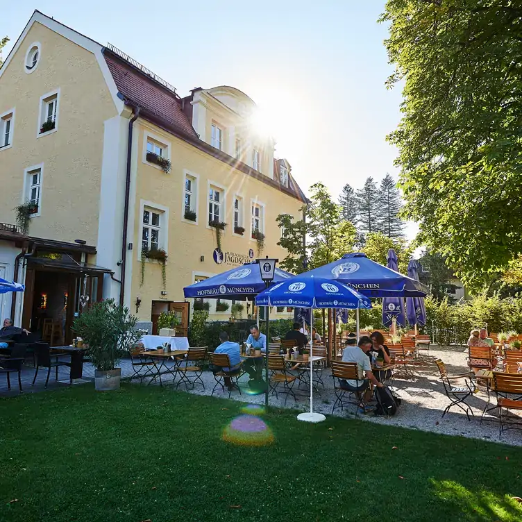 Außenbereich des Harlachinger Jagdschlössel mit Sitzgelegenheiten und schattenspendenden Bäumen, einer der schönsten Biergärten Münchens.