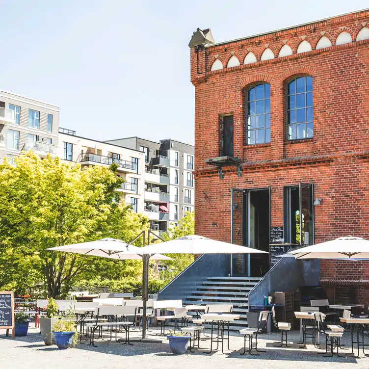 Das rote Backsteingebäude der Blauen Blume von außen mit Sitzgelegenheiten und Sonnenschirmen im Biergarten in Hamburg.