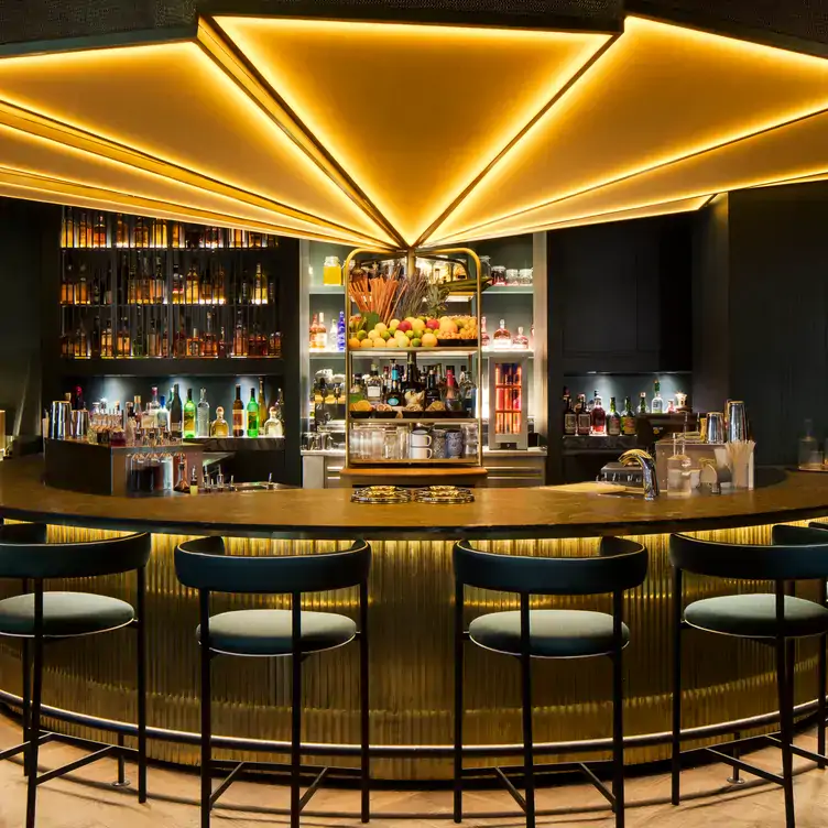 Interior shot of the bar area of Ory Bar, one of the best bars in Munich, showing a semi-circular lit-up bar with drinks and bar stools.