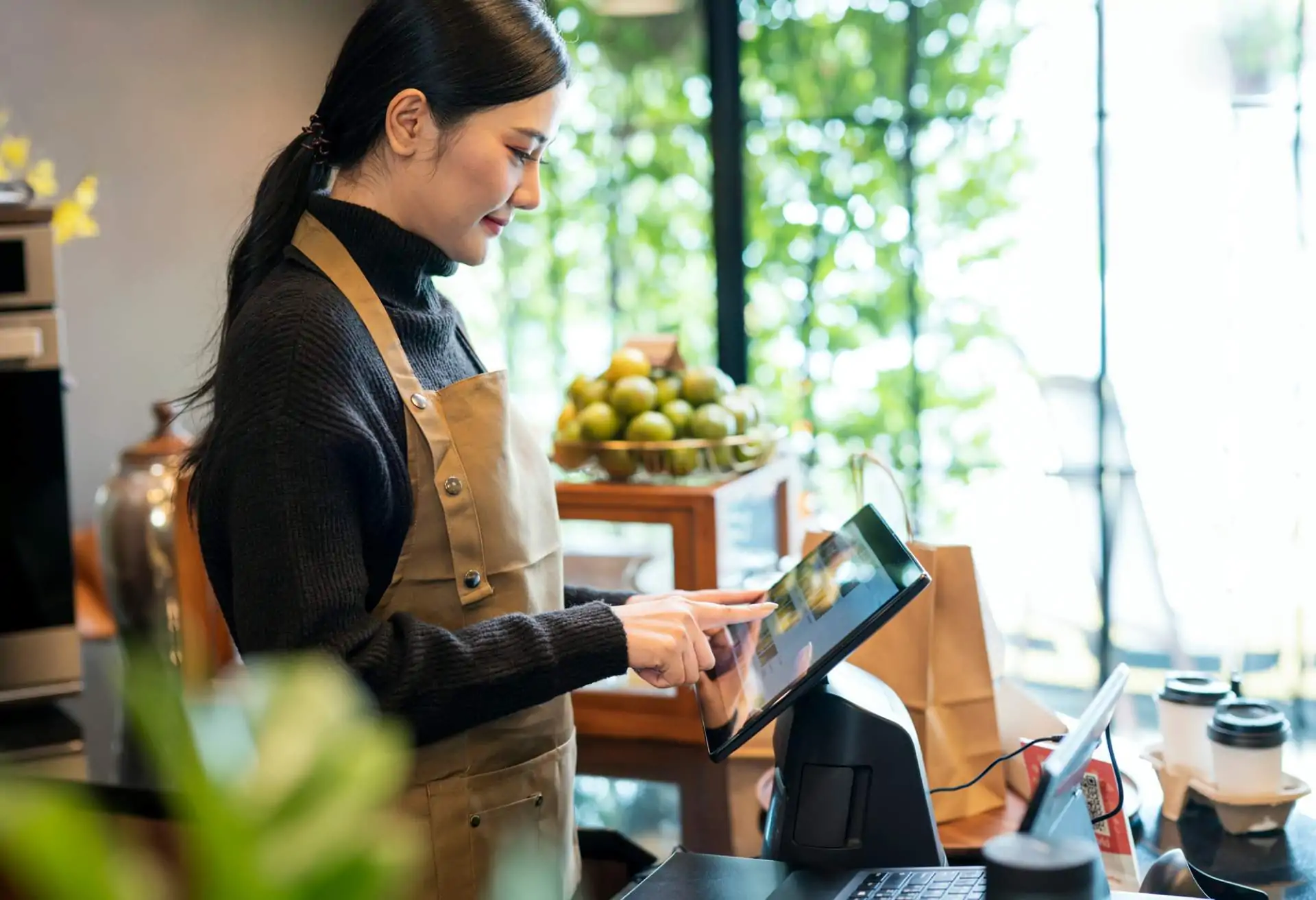 Bild einer Frau mit schwarzem Rollkragenpullover und brauner Schürze, die in einem Restaurant ein fest installiertes Tablet nutzt.